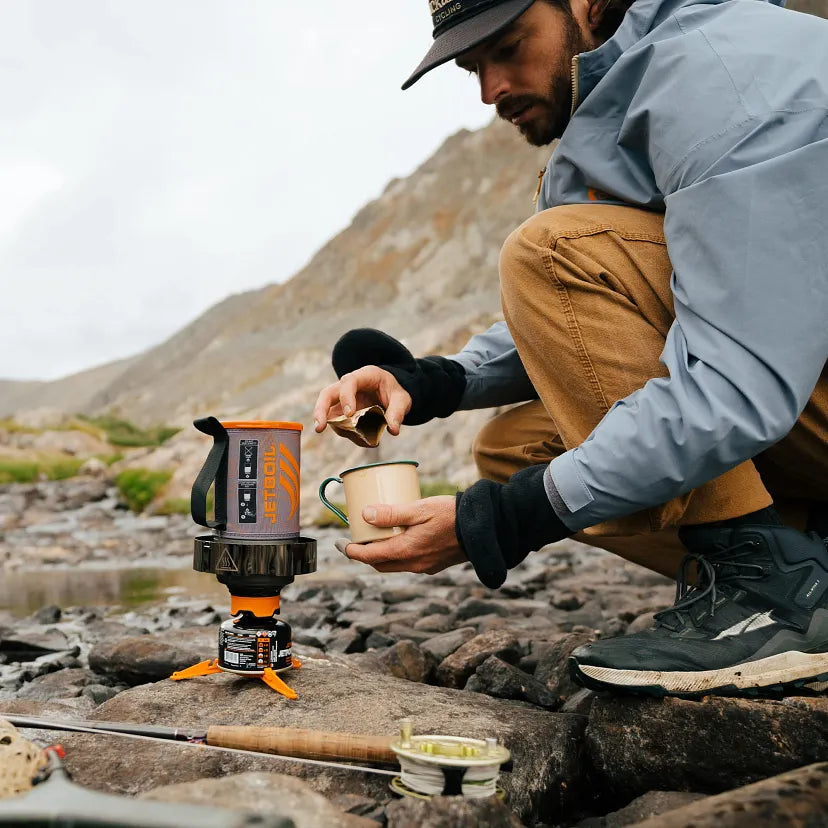 Person camping outdoors, using a portable stove to cook.