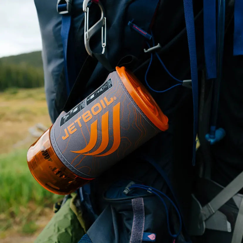 Jetboil camping stove attached to a backpack with a natural landscape in the background