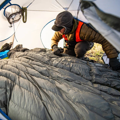 A backcountry hunter positioning a Stone Glacier 15 Degree Chilkoot Sleeping Bag as he enters his tent.