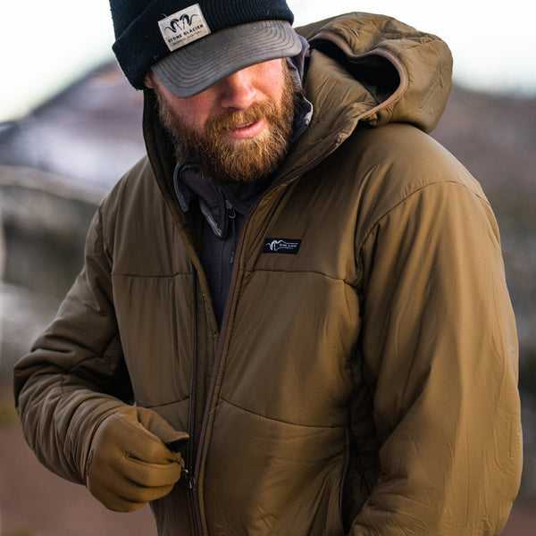 A backcountry hunter zipping up his Stone Glacier Cirque Jacket in muskeg.