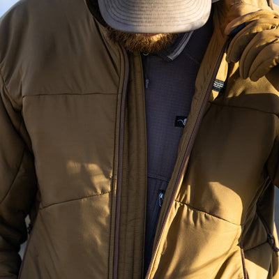 A man unzipping his Stone Glacier Cirque Jacket in muskeg while looking downward.