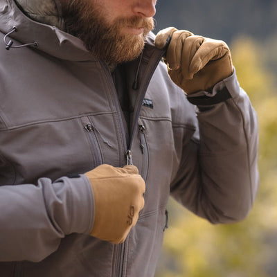 A close-up image of a man wearing and unzipping the Stone Glacier De Havilland Jacket in granite grey.