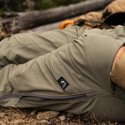 A close-up of a backpacker resting alongside a downed tree while wearing the Stone Glacier De Havilland LITE Pant in tarmac.