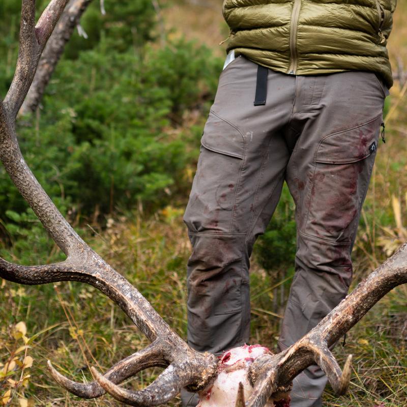 A close-up image of a hunter holding a bull elk on the side of the mountain while wearing the Stone Glacier DeHavilland Pants in granite grey.