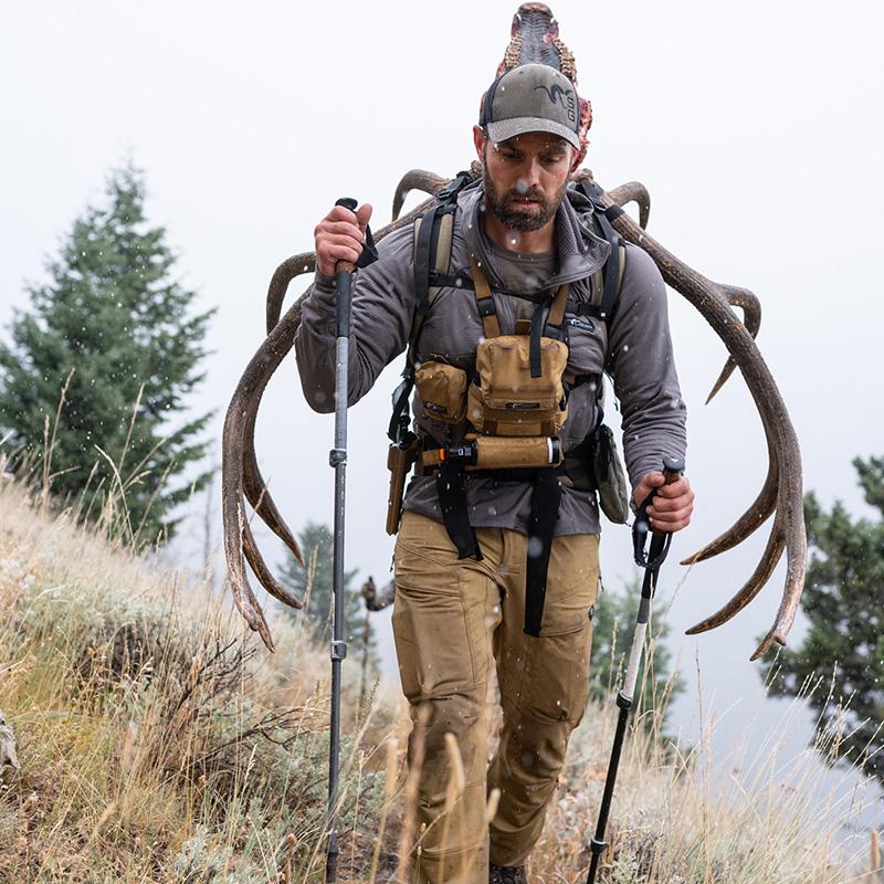 A backcountry elk hunter packing out a bull elk with his backpack while wearing a Stone Glacier Helio Hoody in granite grey.