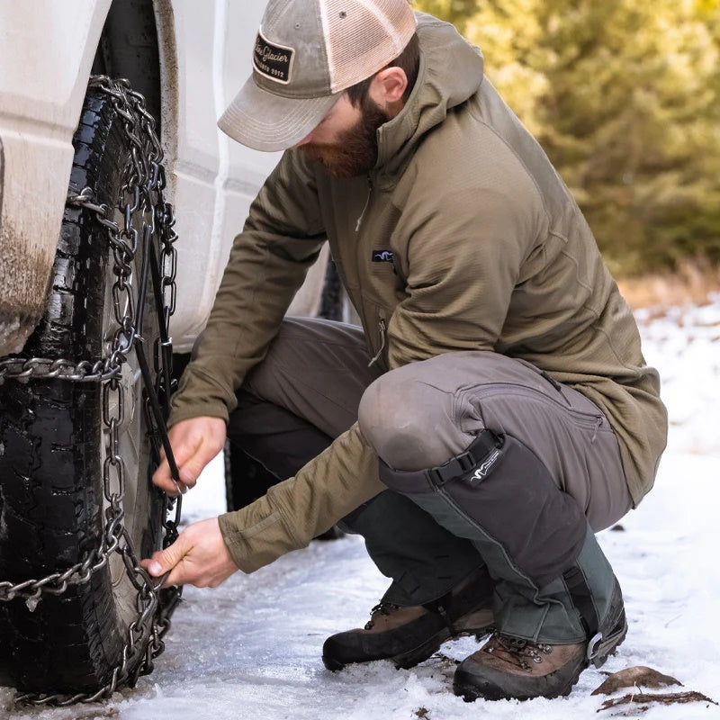 A backcountry adventurer installing snow chains on a pickup truck while wearing the Stone Glacier Helio Hoody.
