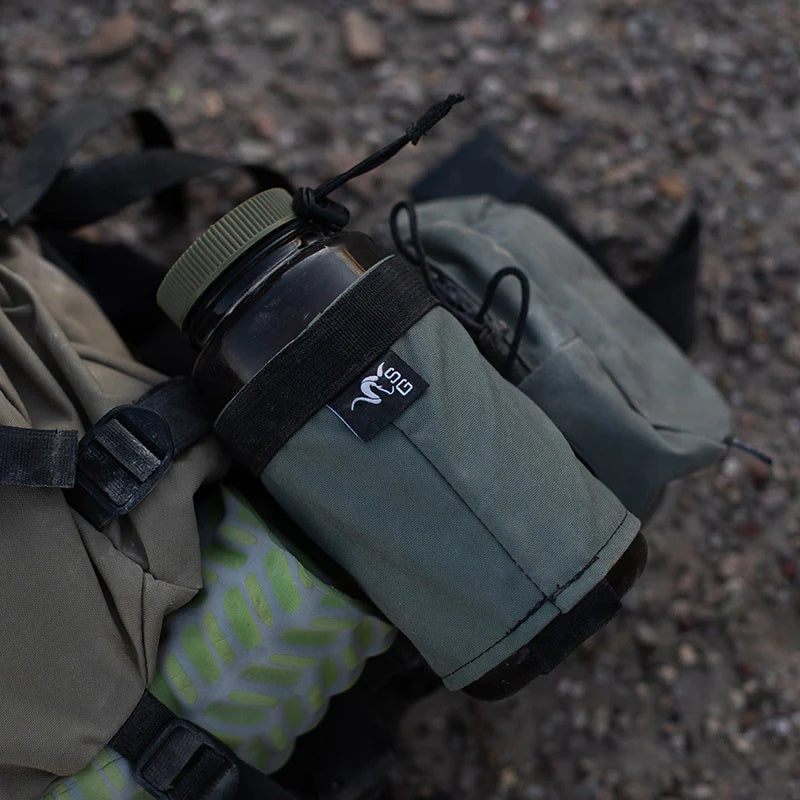 A backpack lying loosely on top of a granite rock with a Stone Glacier Hydro Holster installed and a Nalgene bottle positioned within.