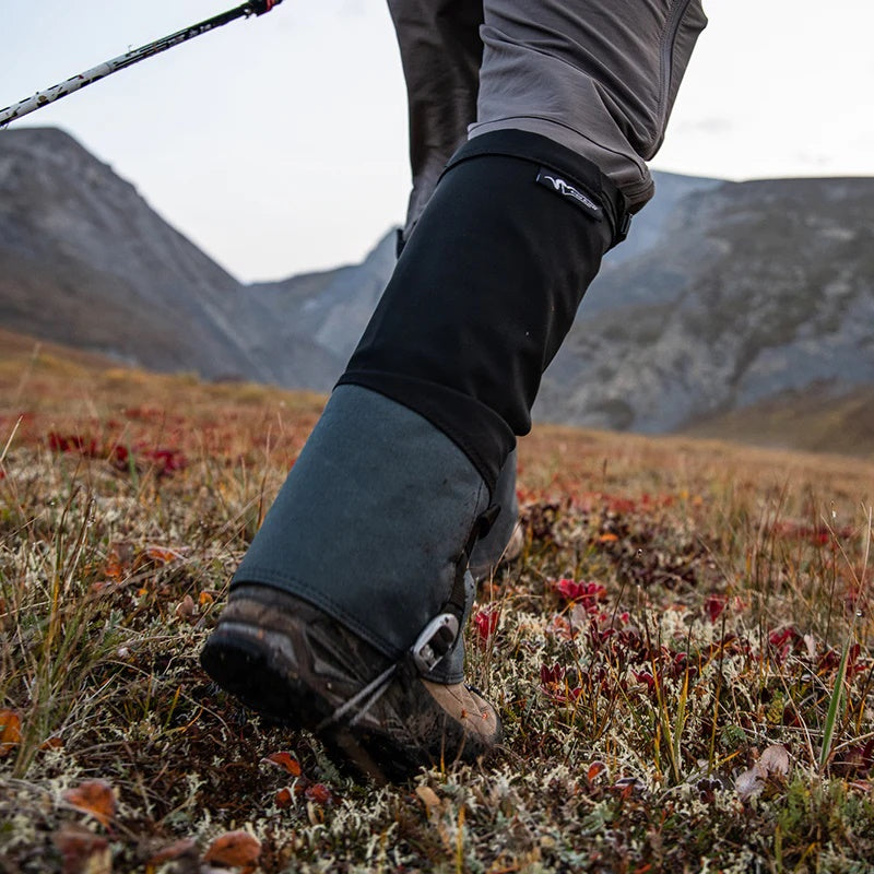 A backcountry hunter traversing a mountain with trekking poles while wearing the Stone Glacier SQ2 Alpine Gaiters.