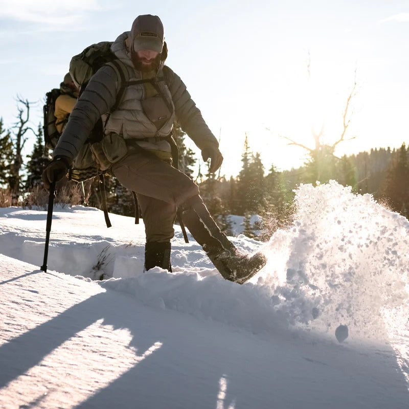 A backcountry hunter in kicking forward through knee deep snow while wearing the Stone Glacier SQ2 Alpine Gaiters.