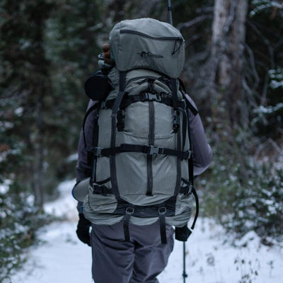 A backcountry hunter walking through the snowy woods while wearing the Stone Glacier Sky 5900 Backpack.